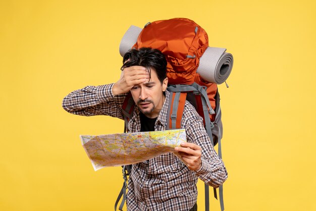 Front view young male going in hiking with backpack observing map on a yellow background company trip nature campus forest color air