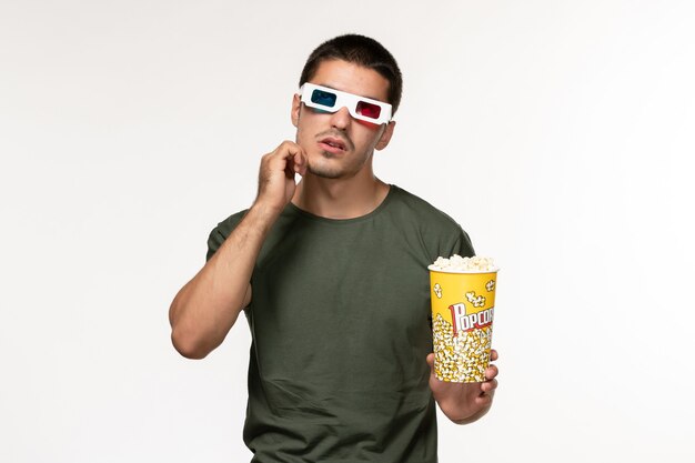 Front view young male in green t-shirt holding popcorn in d sunglasses watching movie thinking on white wall film lonely cinema male movies