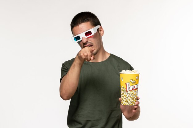 Front view young male in green t-shirt holding popcorn in d sunglasses watching movie on white wall film lonely cinema movie