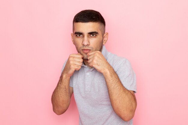 Front view young male in grey shirt standing in the boxing stand on pink