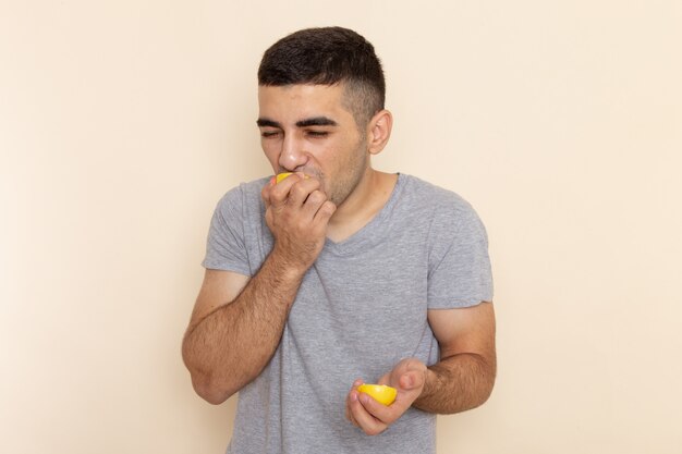 Front view young male in grey t-shirt eating lemon on beige