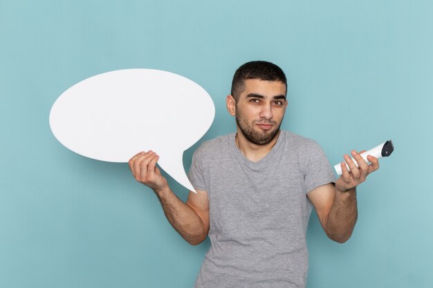 Front view young male in grey t-shirt holding electric razor with white sign on the ice-blue