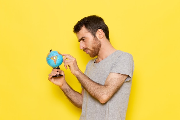 A front view young male in grey t-shirt holding little globe on the yellow wall man color model emotion clothes