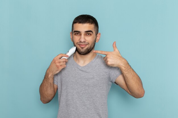 Front view young male in grey t-shirt shaving his beard on the ice-blue shaving beard male hair foam