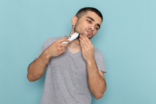 Front view young male in grey t-shirt shaving his beard on iced-blue shaving beard male hair foam