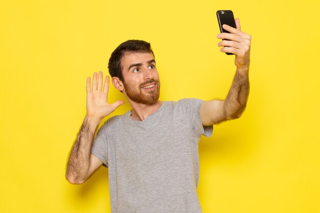 A front view young male in grey t-shirt taking a selfie on the yellow wall man expression emotion color model