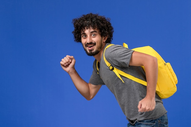 Free Photo front view of young male in grey t-shirt wearing yellow backpack smiling and running on the blue wall