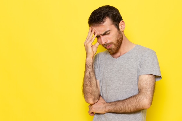 A front view young male in grey t-shirt with thinking expression on the yellow wall man expression emotion color