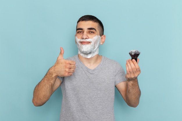 Free Photo front view young male in grey t-shirt with white foam on his face holding brush on iced-blue