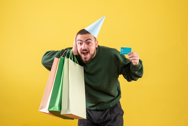 Front view young male holding bank card and shopping packages on yellow