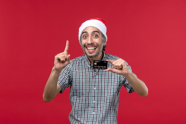 Front view young male holding bank card with smile on red background