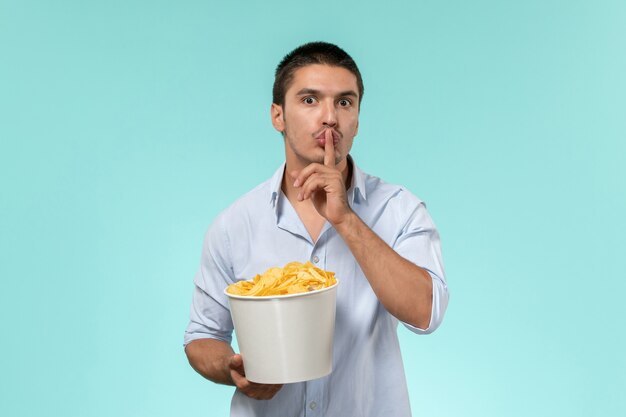 Front view young male holding basket with potato chips and asking to be silent on a blue surface