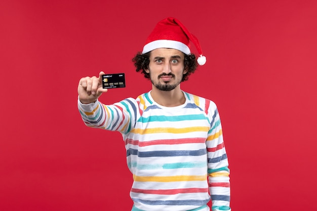 Free photo front view young male holding black bank card on a red wall new year money red holiday