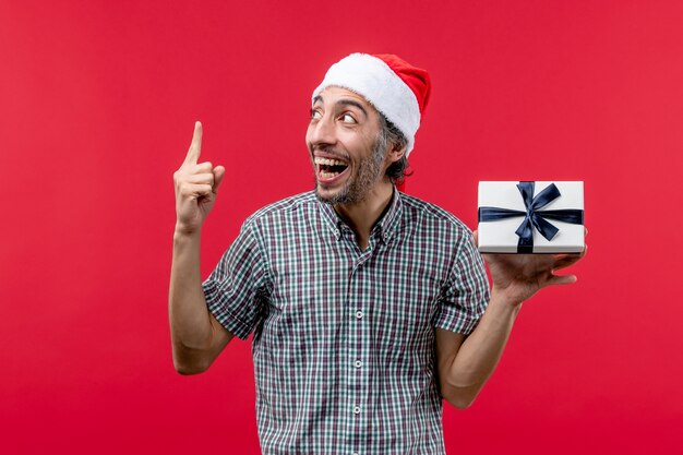 Front view of young male holding Christmas present on red