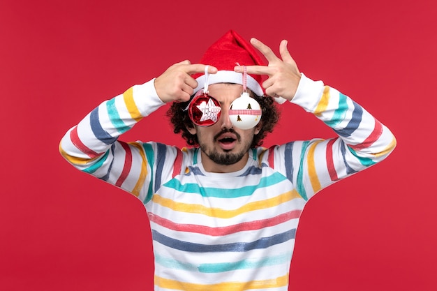 Free Photo front view young male holding christmas tree toy on a red wall new year red holiday