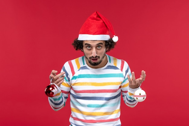 Free Photo front view young male holding christmas tree toy on red wall red model new year holiday