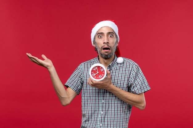 Front view young male holding clocks with scared expression on red background