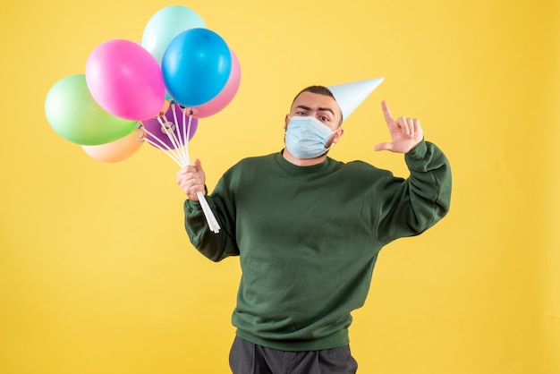 Free photo front view young male holding colorful balloons on a yellow background