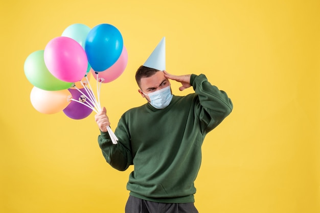 Front view young male holding colorful balloons on yellow background