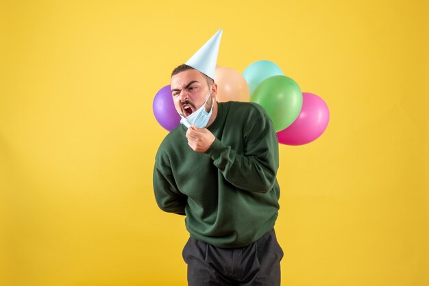 Front view young male holding colorful balloons on yellow desk