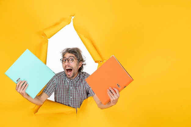 Free photo front view of young male holding files on a yellow wall