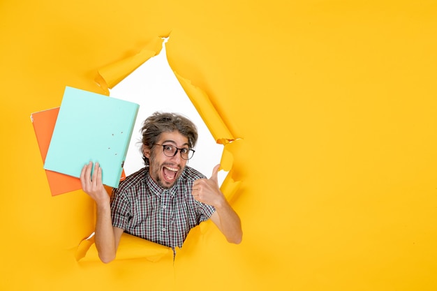 Free photo front view of young male holding files on a yellow wall