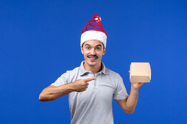 Front view young male holding food package on a blue wall food male service job