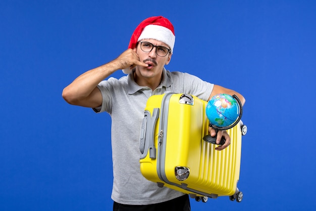 Front view young male holding globe and yellow bag on blue wall plane vacation trip