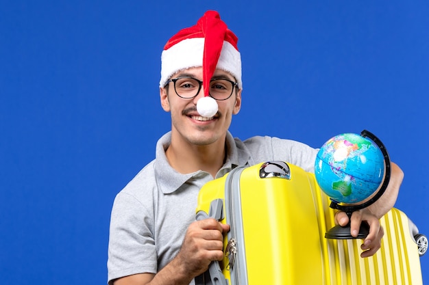 Front view young male holding globe and yellow bag on a blue wall planes vacation trip