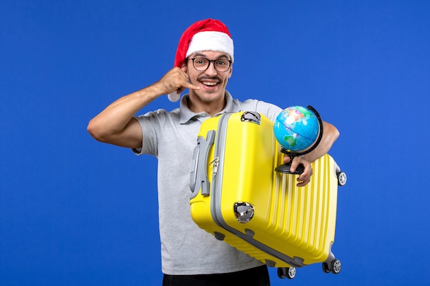 Free Photo front view young male holding globe and yellow bag on blue wall planes vacation trip