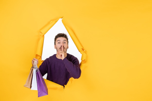 Free photo front view young male holding little packages after shopping on a yellow background gift new year present xmas color holiday