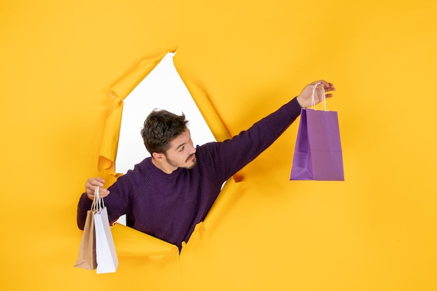 Free photo front view young male holding little packages after shopping on yellow background new year color holiday gift xmas