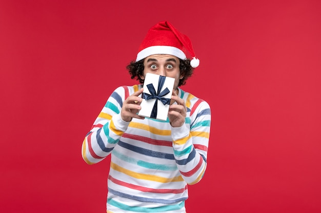 Free photo front view young male holding new year present on red desk holiday new year emotions