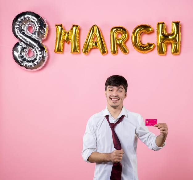 Free photo front view young male holding pink bank card with march decoration on pink background party present holiday man feminine money equality color shopping