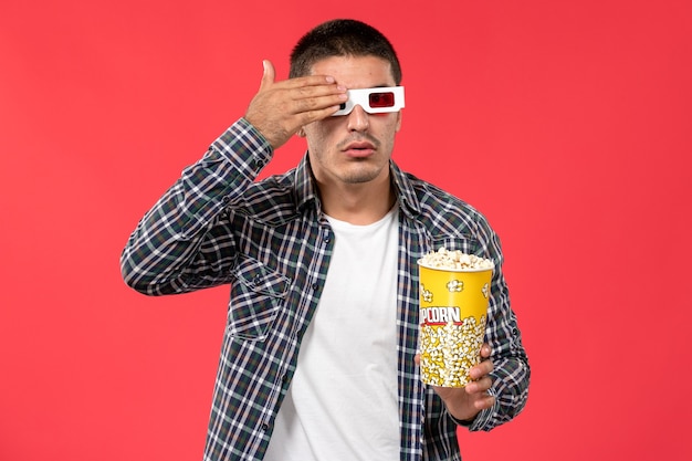 Free Photo front view young male holding popcorn package in -d sunglasses on light-red wall cinema movie theater film male