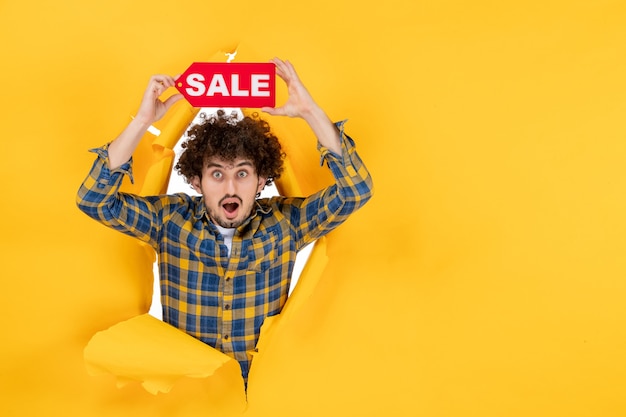 Front view young male holding red sale writing on a yellow ripped background