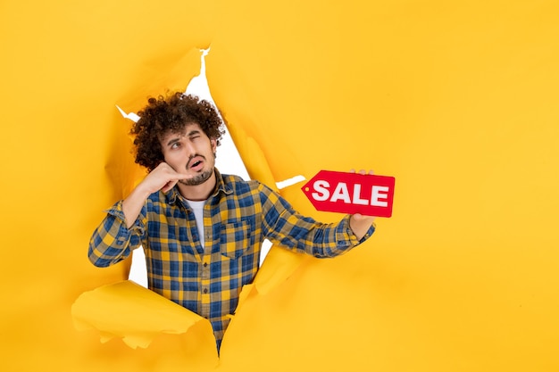 Free Photo front view young male holding red sale writing on a yellow ripped background