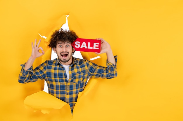 Free Photo front view young male holding red sale writing on the yellow ripped background