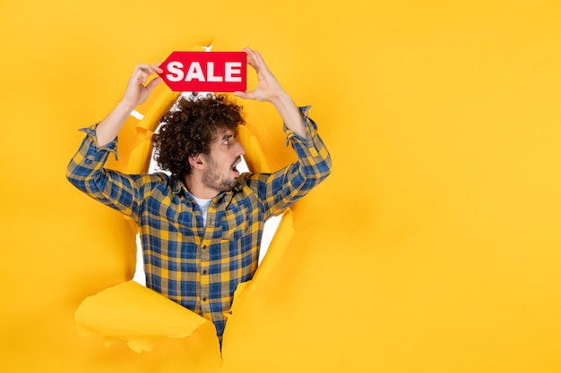 Front view young male holding red sale writing on yellow ripped background