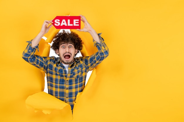 Free Photo front view young male holding red sale writing on yellow ripped background