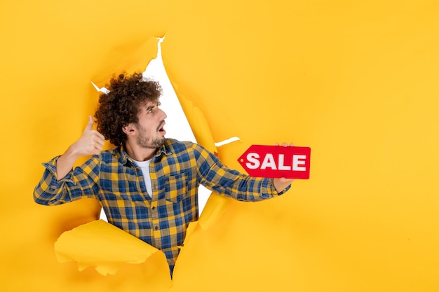 Free photo front view young male holding red sale writing on yellow ripped background