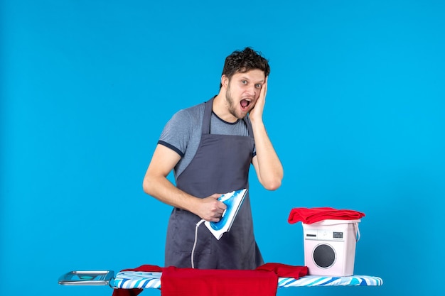 Free photo front view young male ironing red shirt on blue surface