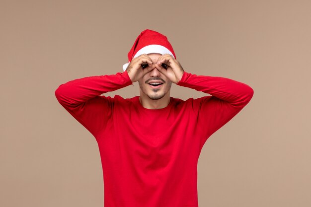 Front view young male looking through fingers on brown background christmas holiday emotions