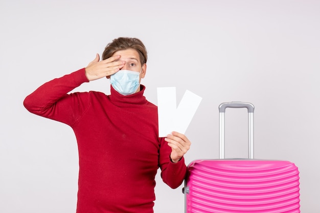 Free photo front view of young male in mask holding plane tickets on the white wall