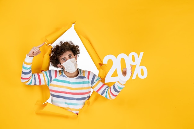 Free photo front view young male in mask holding writing on yellow coronavirus health covid- sale color photo