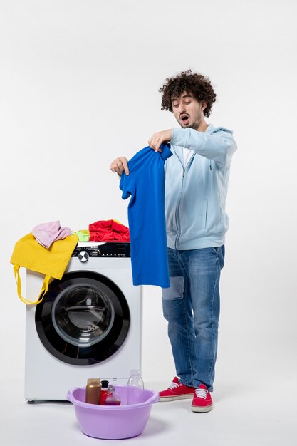 Front view of young male preparing dirty clothes for washer on white wall