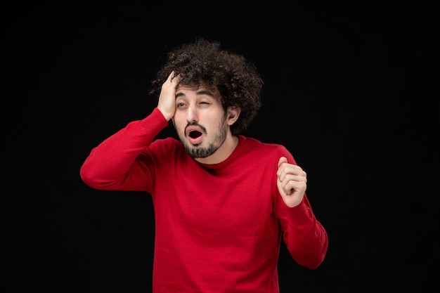 Front view of young male in red shirt on black wall