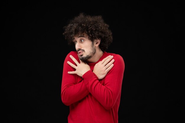 Front view of young male in red sweater on the black wall