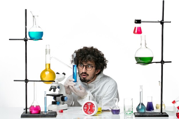 Front view young male scientist in special suit holding flask with solution on a white wall