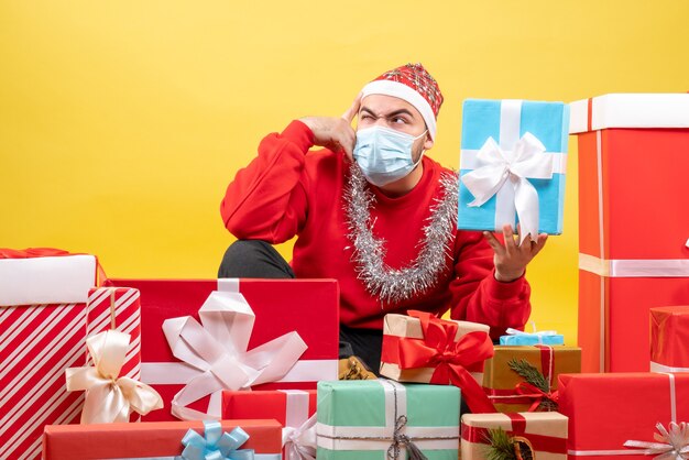 Front view young male sitting around christmas presents on the yellow background